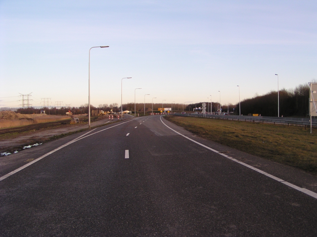 p1130022.jpg - Diverse evolutiestadia van het A58 begin bij Eindhoven. Links de A58 noordtak die werd aangelegd in de tachtiger (?) jaren om aan te sluiten op de verlengde Kennedylaan, als vervanging van de in 1977 aangelegde vloeiende boog naar de Kennedylaan. Ook de rechter (zuid) tak dateert uit dat tijdperk en is thans tijdelijk verbreed om beide rijrichtingen te bedienen. In het midden de pas enige jaren geleden gerealiseerde verlegde noordtak, dicht tegen de zuidtak aangelegen, bedoeld om blokkades door foutief opgestelde voertuigen voor de VRI's te voorkomen. De reden voor de oorspronkelijke ruimtereservering tussen noord- en zuidtak is mij niet bekend; wellicht had men hier destijds op doortrekking van de A58 naar het oosten gehoopt.