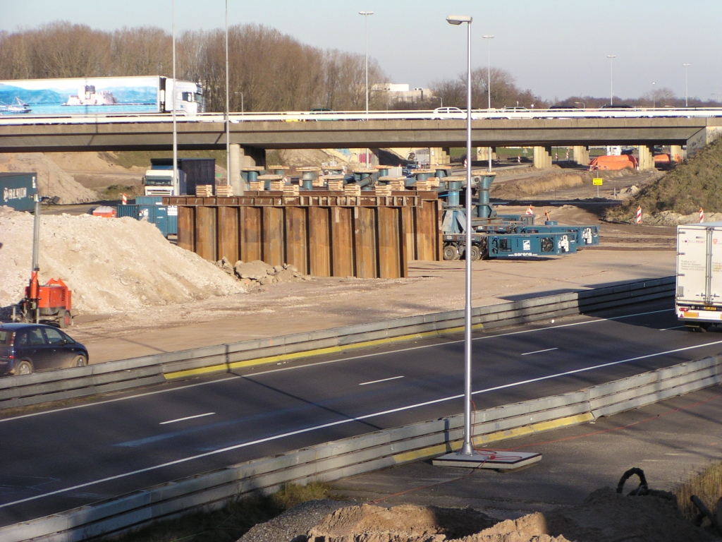 p2150004.jpg - De laatste rustplaats van het viaduct, waar het ter beschikking van de recycling zal worden gesteld: drie evenwijdige rijen damwanden op precies dezelfde afstanden als de oorspronkelijke pilaren. Net zichtbaar de platform carriers van de firma Sarens die de uitvaart zullen verzorgen.