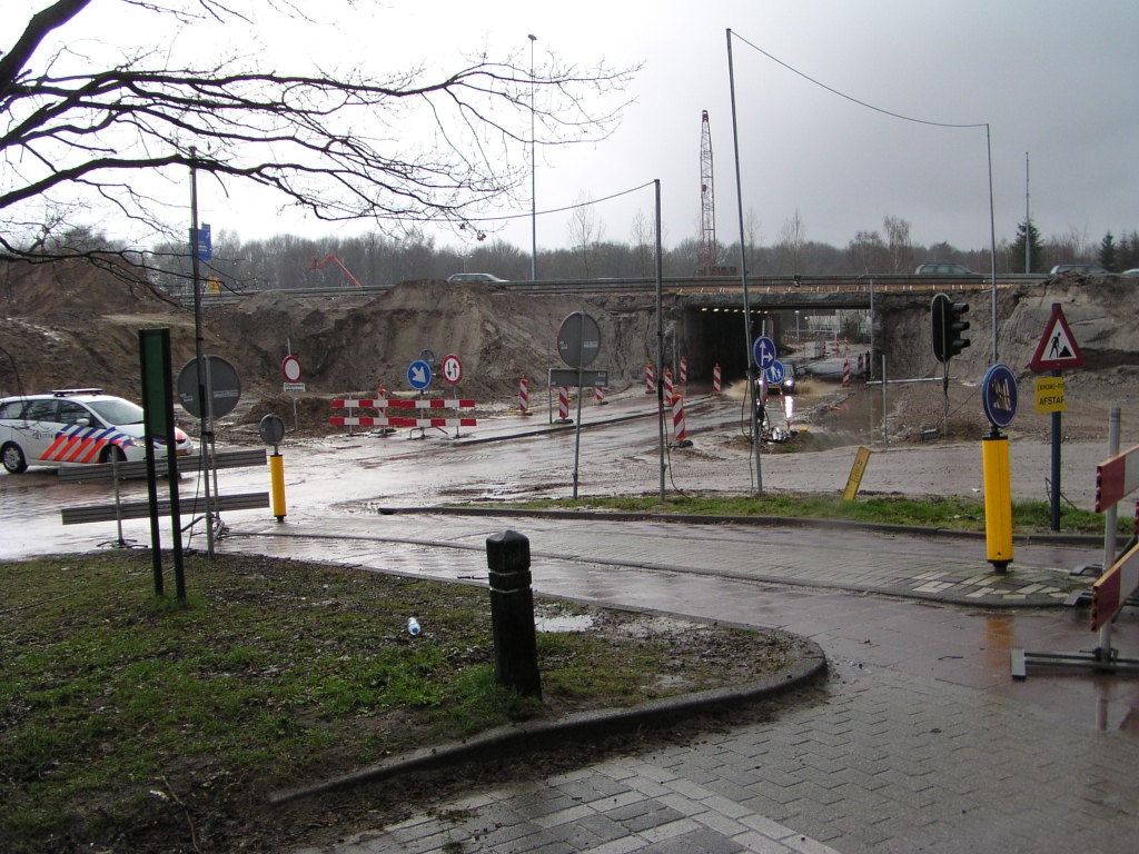 p3160054.jpg - Bij het voorlopig eindpunt van de parallelbaan omlegging gutst het regenwater van het tunneltje Welschapsedijk af. De politie houdt een oogje in het zeil terwijl voertuigen door de plassen ploegen.