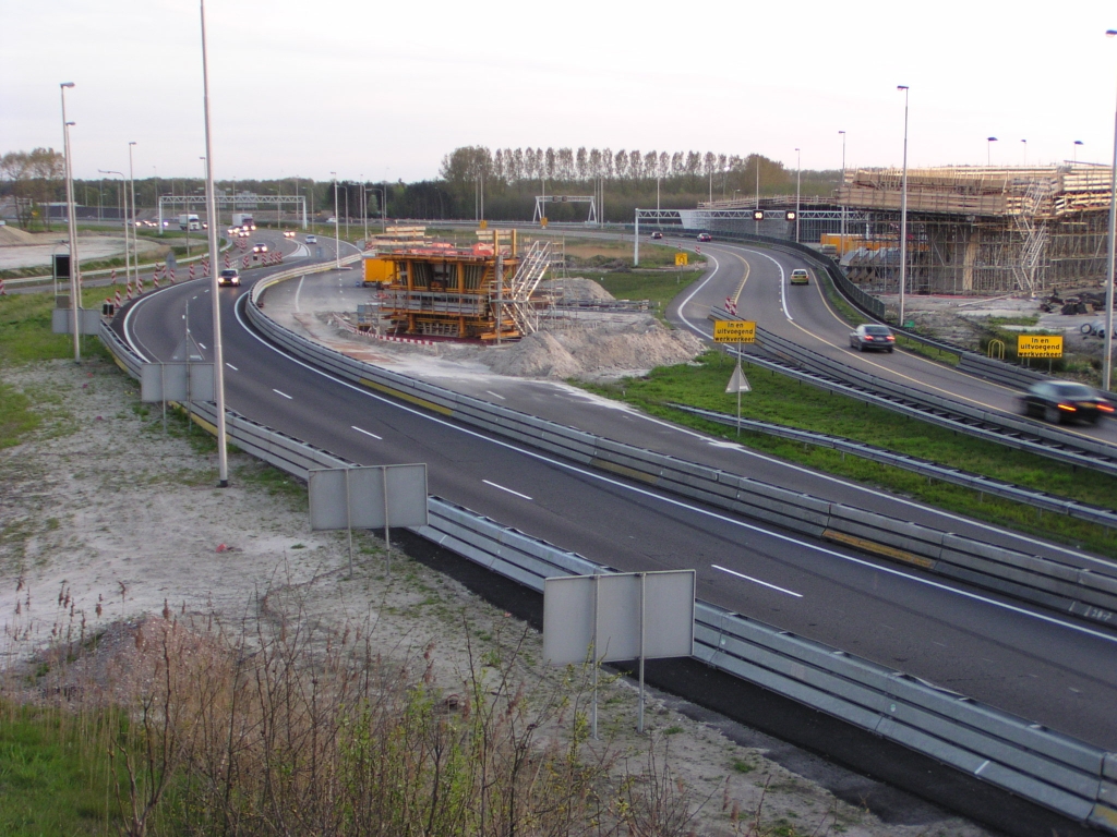 p4260144.jpg - Weer zo'n positie die we al veel eerder in de fotoreeksen hadden moeten opnemen als vast observatiepunt in kp. Batadorp. Rechts een gedeelte van KW 4C, waaronder de parallelbaan beschikbaar komt als het eenmaal gestort is. Hetzelfde geldt voor KW 5 daarachter. Zodoende kan het verkeer dat nu nog op de oude A2 hoofdrijbaan rijdt worden overgezet naar de parallelbaan onder KW's 4C en 5. De vrijkomende ruimte kan dan worden benut om de volgende moot in KW 4C te realiseren, als die steun in gele bekisting gereed is. We zien in dat verband het nut van het verleggen van de bestaande verbindingsweg richting Tilburg. Verder fantaserend over ons faseringsplan, zien we die verlegging verplaatst worden naar de rechterkant van de gele pilaar, als die tweede moot in KW 4C gereed is. Vervolgens kan KW 4C worden gecompleteerd. Tegen die tijd zijn ook KW 4A en 4B gereed, zodat het verkeer Tilburg->Amsterdam/Nijmegen kan worden overgezet. Hierdoor raakt de zuidelijke rijbaan van de A58 door kp. Batadorp vacant, zodat de nieuwe rijbaan vanaf de Randweg naar Tilburg, over het inmiddels gecompleteerde KW 5, kan worden aangesloten op de noordelijk rijbaan van de A58. Enzovoorts :-) Het is leuk deze tekst over een jaar nog eens terug te lezen als gebleken is dat het compleet anders is verlopen.