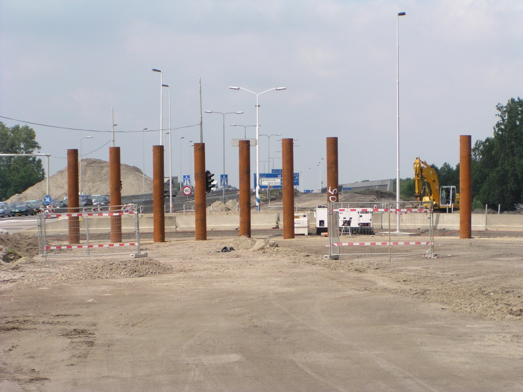 p6010040.jpg - Niet de vertrouwde heipalen bij de start van de bouw van een nieuw viaduct, maar stalen pijpen. Zou het net zoiets worden als de  brug over het Wilhelminakanaal , waar het landhoofd opgetrokken is uit zulke pijpen, gecombineerd met damwanden? De rechtse pijp staat wat verder weg, zodat het vermoeden is dat er daar een tweede viaduct komt...