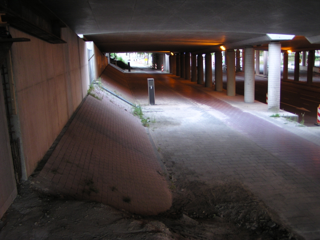 p7060075.jpg - Om de doorrijhoogte te vergroten drukt men een damwand in en graaft het gedeelte rechts daarvan tot aan de viaductsteunen af. Voor een enkele rijstrook zou die damwand onderaan het klinkertaludje kunnen staan. Misschien dat twee rijstroken, nodig voor de ontvlechtingsvariant, gerealiseerd kunnen worden door de damwand pal tegen het linker landhoofd te plaatsen?