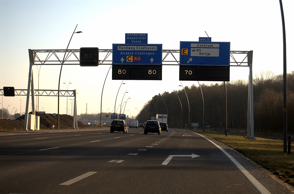 20081213-124213.jpg - Zoals gebruikelijk bij de openstelling van nieuwe wegvakken in de Randweg Eindhoven een Vmax van 70. Goed te zien ook in de drive-by opname dat de borden tijdelijk een stukje naar rechts zijn verschoven. Als rijstrook 3 eenmaal is omgezet naar tweede uitvoegstrook, kan het solitaire matrixbord uiterst links worden verwijderd en de hele handel naar links worden verplaatst. Merkwaardige gedeeltelijke afplakking van de industrienummering.  week 200848 