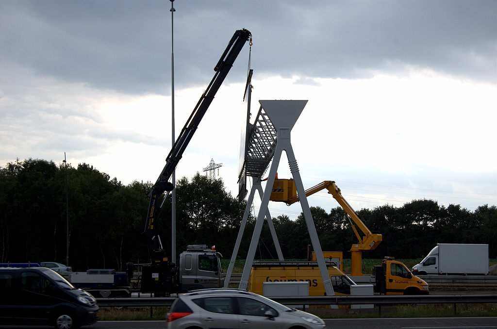 20090709-143231.bmp - Bij het inhaken van het bord komt de man in de hoogwerker nog niet te pas. Het karwei wordt geklaard door een kraandrijver en twee mannen die met touwen manoevreren.