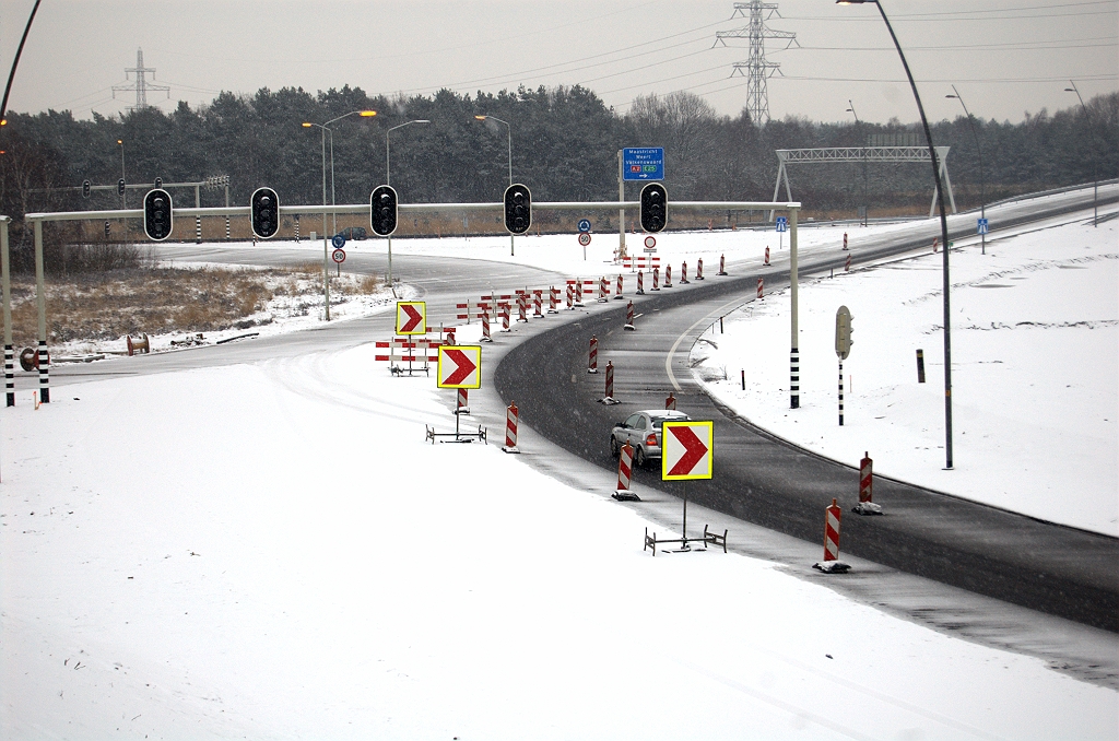 20100214-171432.bmp - Vijf opstelstroken dus voor al het verkeer dat zich vanaf vijf afritten heeft geaccumuleerd en zijn reis wil vervolgen naar de A67 in de richting Venlo of de A2 in de richting Maastricht. Dat zijn er nog altijd twee meer dan in de situatie voor 1996, toen de bypass er nog niet was en ook het doorgaande A2 verkeer over de rotonde moest. We pakken alvast onze zakdoek voor de tragedie zie zich aan de mast in de achtergond heeft afgespeeld.