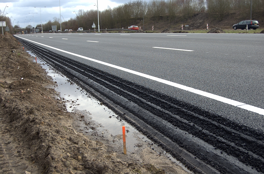 20100321-162401.bmp - Aan de andere zijde van de rijbaan werden twee rijstroken toegevoegd voor de toerit naar de A50 in de richting Nijmegen. We zien hier dan ook vier nieuwe onderlagen en ZOAB deklaag.