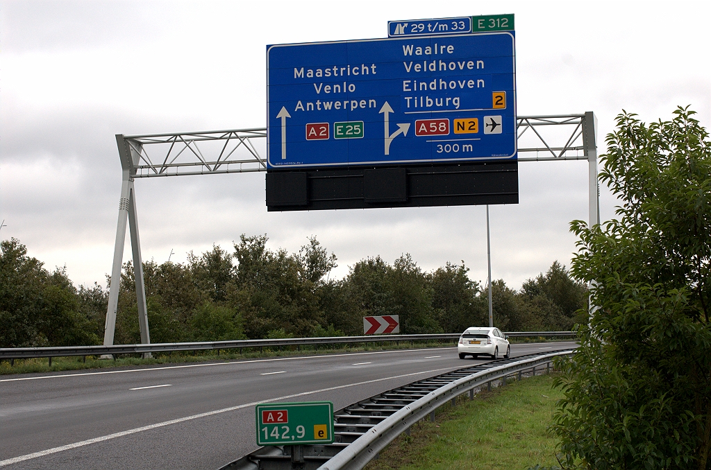 20101016-132659.bmp - Eerste portaal op het wegvak waar het er echt toe doet: keuze hoofd- en parallelrijbaan. Tilburg een regel naar beneden verplaatst, en Eindhoven op de vrijkomende derde regel. Vliegveldsymbooltje dit keer niet achter het het doel Eindhoven, maar bij de wegnummerschilden. Daar is nu geen ruimte meer voor de E312, die naar een ruitertje verhuisd is.  week 201017 