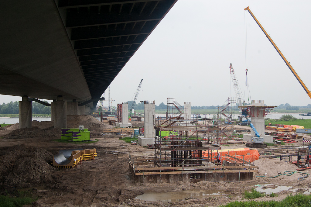 20110803-142826.jpg - Nog even terugkijken op de noordelijke uiterwaarden, waarvan het aanzicht vooral gedomineerd wordt door de betonnen kolommen die dienen als ondersteuning bij het inschuiven van het brugdek en uiteindelijk weer worden verwijderd. Aardig wel dat de permanente steunen dezelfde ovale vormgeving hebben als die onder de oude brug, maar ze staan niet op dezelde afstanden. Hun aantal wordt vast ook groter, omdat een betonnen brug zwaarder is dan een stalen, zo gokken we.