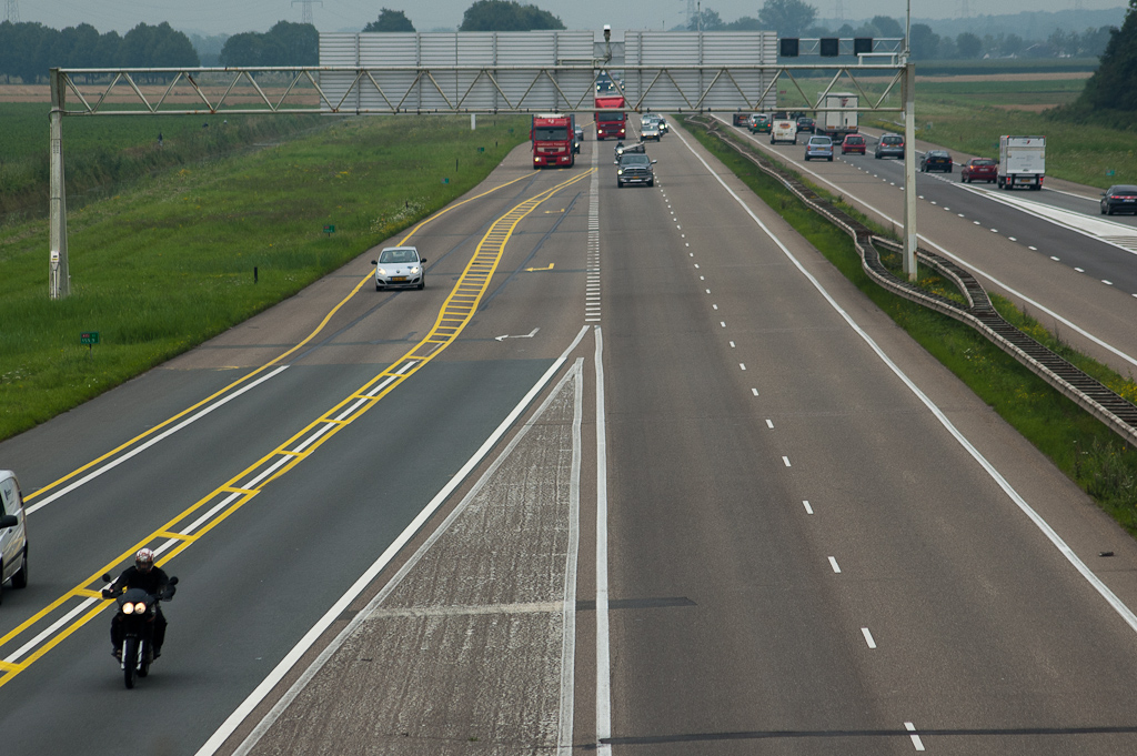 20110803-145543.jpg - Je moet nu dus op de hoofdrijbaan al kiezen of je, komende vanuit de richting Ressen, naar Eindhoven of Apeldoorn wil. Fotograaf besloot daarop zijn chauffeuse op de proef te stellen. Zij nam zo vroeg mogelijk de uitvoegstrook, ook al wilde ze naar Eindhoven, en overschreed zonder pardon de dubbele doorgetrokken gele strepen om op de rangeerbaan naar de klaverlus te geraken.