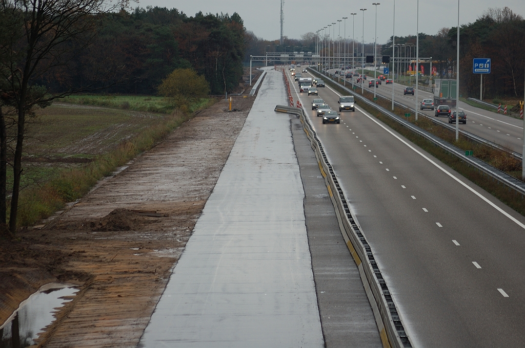 20101114-145912.JPG - Twee weken geleden eindigde het verbredingsasfalt nog in een grasstrook aan de oostzijde van het viaduct Eindhovensedijk. Thans is het doorgetrokken en ZOAB-gereed. Tevens nieuwe bermsloot op de voorgrond. Het verder van de rijbaan gelegen slootje was er al, maar door begroeing aan het zicht onttrokken. Geleiderail vanaf de verzorgingsplaats Kriekampen lijkt te eindigen bij dat slootje, zodat het kennelijk op "obstakelvrije" afstand is gelegen. Bij de nieuw aangelegde sloot verwachtten we dan de hervatting van de geleiderail.  week 201043 