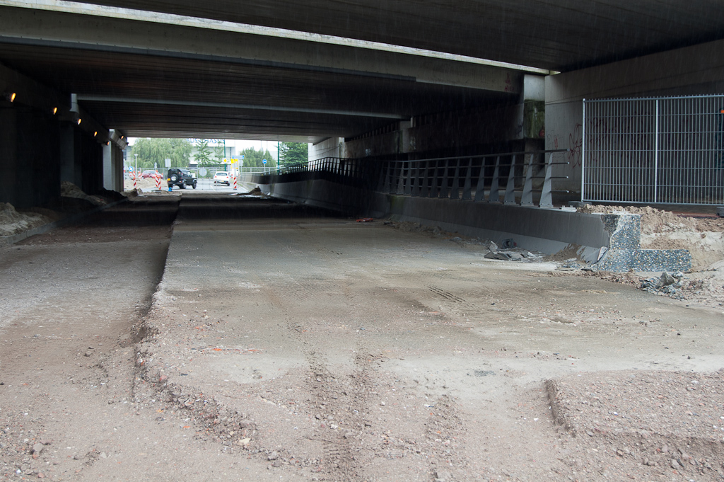 20110619-153039.jpg - Onder het viaduct is het leidingenwerk voltooid, de sleuf weer dichtgegooid en voorzien van puinfundering (links) voor de derde rijstrook, een opstelvak naar de toerit in de richting Amsterdam. Rechts de afgezaagde betonnen kering waar we een soortgelijke overgang verwachten als  aan de andere (noord-)zijde .