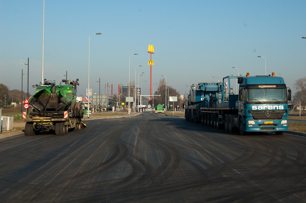 20111120-142421.jpg - Enige rijbaan in de periferie van de Hovenring die nog niet is voorzien van een deklaag vinden we in de Noord-Brabantlaan, noordzijde. Opgestelde asfaltspreider lijkt een teken dat daar snel verandering in komt. Mobiele kraan rechts staat wellicht al klaar voor het volgende transport van de brugdelen.